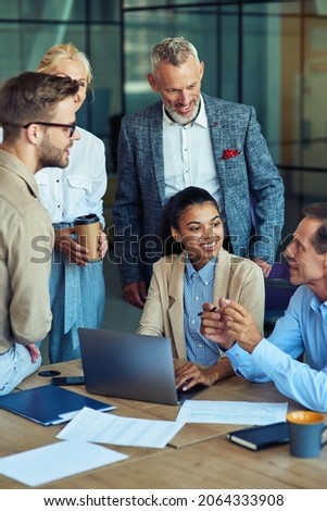 Cheerful multiracial business team using laptop, discussing project results and smiling while having a meeting in the modern office, working together Royalty-Free Stock Photo #2064333908