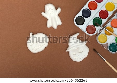 Halloween crafts. Gibs figurines of pumpkins and ghosts in bright paint with a brush on a brown background, ready for drawing close-up