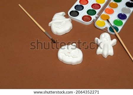 Halloween crafts. Gibs figurines of pumpkins and ghosts in bright paint with a brush on a brown background, ready for drawing close-up