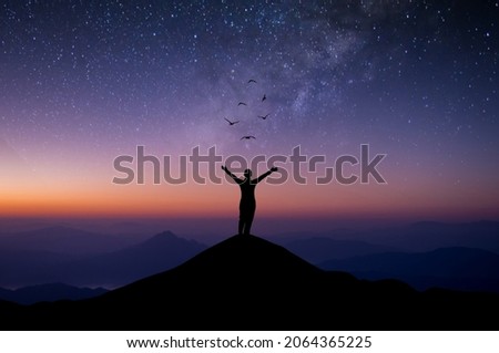 Silhouette of young woman standing alone on top of mountain and raise both arms praying and free bird enjoying nature on beautiful night sky, star, milky way background. Demonstrates hope and freedom. Royalty-Free Stock Photo #2064365225