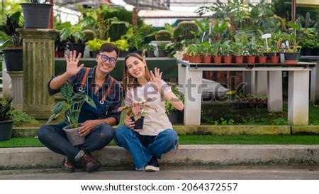Asian couple gardener caring houseplant and flowers in greenhouse garden together. Man and woman plant shop owner working in potted plants store. Small business entrepreneur and plant caring concept.