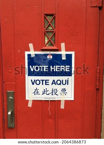 Blue and white "Vote Here Vote Aqui" voting sign in English, Spanish and Chinese languages taped to red school door in New York City