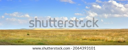 A wide plain in autumn, hills on the horizon under a cloudy blue sky. Siberia, Russia
