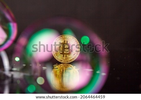 Golden bitcoin coin standing on a reflective desk surface.