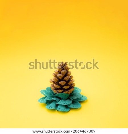 Pinecone on a green textile flower. Yellow background. Minimal Christmas design and new year season concept.