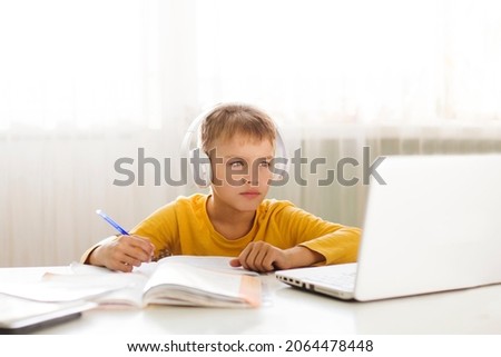 schoolkid in headphones is using a laptop and study online with video call teacher at home. homeschooling, distant learning