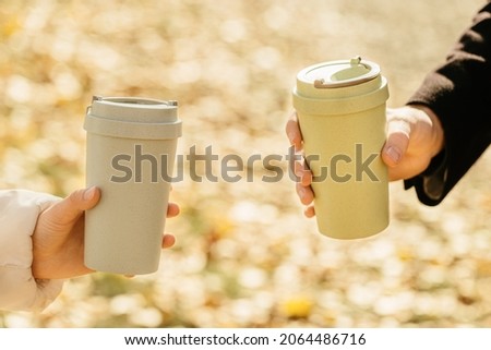 Woman holds in her hand reusable eco coffee cup with lid on autumn blurred  background with bokeh. Zero waste concept. Ban single use plastic. Take away big mug for drinks. Royalty-Free Stock Photo #2064486716