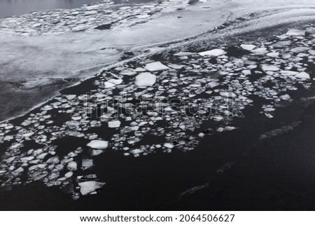 Pieces of thin white ice on dark water. Melting ice in spring. Global warming.
