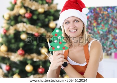 Woman artist in santa hat holding toy christmas tree and paint brushes