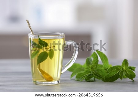 Cup of tea with spoon, green tea leaves and mint on blurred background