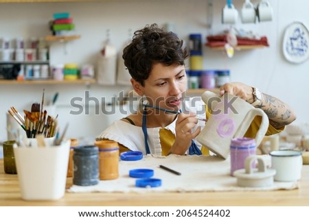 Young creative woman small business owner work in art studio with pottery for handmade shop. Girl relax with painting, ceramics after work create craft kitchenware in workshop. Artistic hobby concept Royalty-Free Stock Photo #2064524402