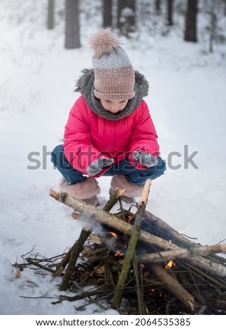 Child in winter. Little girl in winter in nature warms her hands by the fire