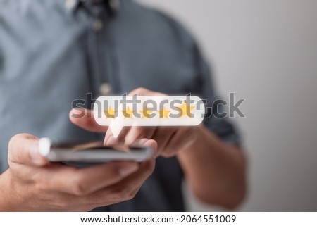 Close-up of a customer hand pressing on a smartphone screen with a gold five-star rating feedback symbol and a press level superb rank for providing the highest possible score to assess the service Royalty-Free Stock Photo #2064551009
