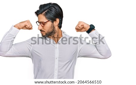 Young hispanic man wearing business shirt and glasses showing arms muscles smiling proud. fitness concept. 