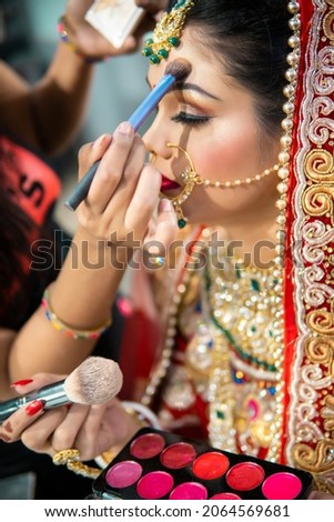Close up of the beautiful traditional Indian bride getting ready for her wedding day. Cropped hand of makeup artist doing a makeup of bridal face and applying lipstick. Royalty-Free Stock Photo #2064569681