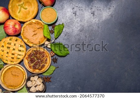 Set variety autumn pies. Pecan, apple, pumpkin small tart cakes and pies on concrete background with bright sun light, dark shadows top view 