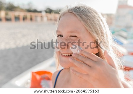 Close-up portrait of a young sweet and happy teenage girl smearing sunscreen on her face.