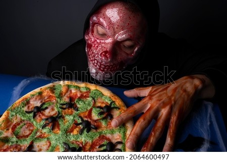 Halloween scary skeleton man portrait with Halloween pizza on grey and blue background 