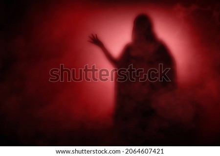 Silhouette of witch woman with a cloak standing with dramatic background