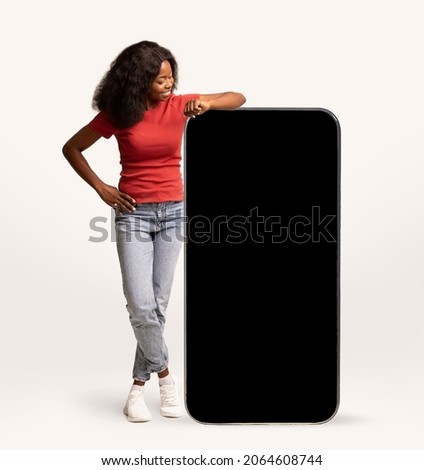 Mobile Ad. Young Cheerful Black Lady Leaning At Big Smartphone With Blank Screen, Smiling African American Woman Demonstrating Free Copy Space For Your Design Or Advertisement, Mockup Image