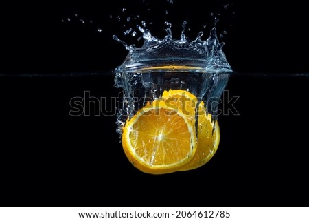 Orange slices falling into water on a black background. Fresh and juicy orange