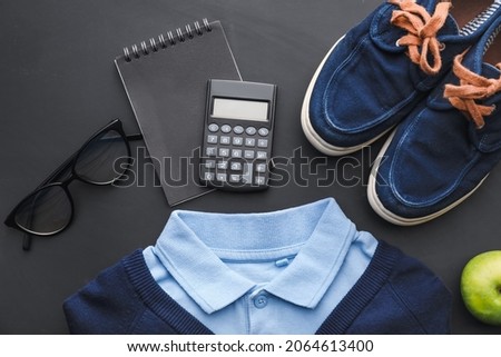Stylish school uniform, shoes, eyeglasses and stationery on dark background, closeup