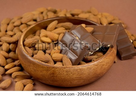 Milk chocolate bar with almonds in a wooden bowl stock images. Almond chocolate in a bowl on a brown background close-up stock images