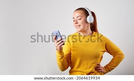 Close up portrait of caucasian female podcast or music listening on grey background. listening music in headphones