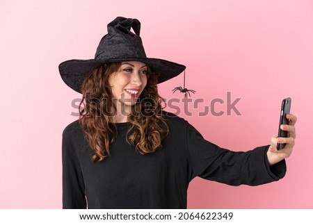 Young caucasian woman celebrating halloween isolated on pink background making a selfie