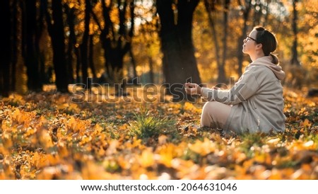 Caucasian middle aged woman meditating in lotus pose at autumn park with sunlight. Yoga at fall park. Woman in glasses relaxing on yellow leaves. Meditation, Mental health, self care, mindfulness Royalty-Free Stock Photo #2064631046