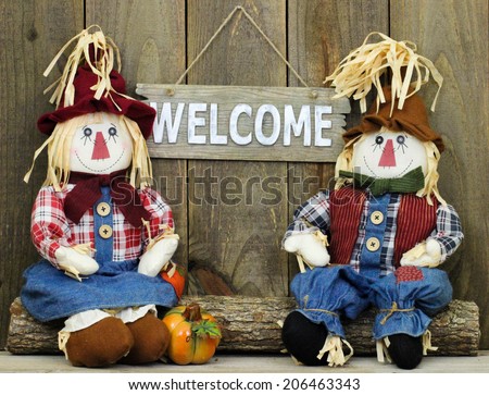 Boy and girl scarecrows sitting on log by rustic wood welcome sign and pumpkin
