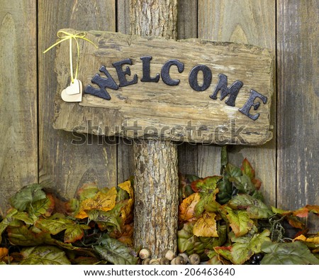 Welcome sign with hearts hanging on tree by fall leaves and acorns