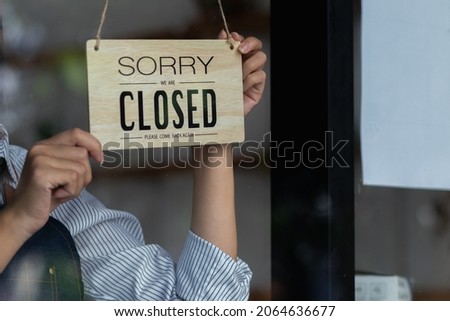 The shop owner puts a wooden sign that says it's closed on the glass door of the shop to tell customers about the time it's closed. Concept of closing stores during the coronavirus pandemic