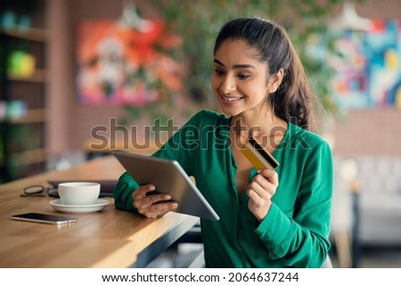 Cheerful millennial indian lady banking online, using digital tablet and credit card at cafe, young woman buying clothes or cosmetics on Internet, using shopping mobile application on pad Royalty-Free Stock Photo #2064637244