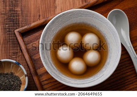 Top view of sesame big tangyuan (tang yuan, glutinous rice dumpling balls) with sweet syrup soup in a bowl on wooden table background for Winter solstice festival food. Royalty-Free Stock Photo #2064649655
