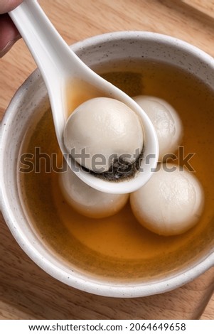 Top view of sesame big tangyuan (tang yuan, glutinous rice dumpling balls) with sweet syrup soup in a bowl on wooden table background for Winter solstice festival food. Royalty-Free Stock Photo #2064649658