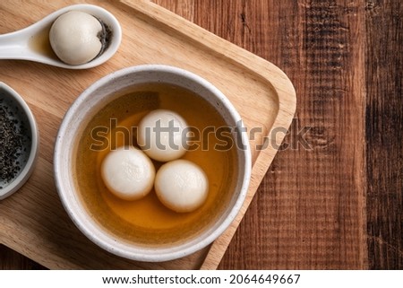 Top view of sesame big tangyuan (tang yuan, glutinous rice dumpling balls) with sweet syrup soup in a bowl on wooden table background for Winter solstice festival food. Royalty-Free Stock Photo #2064649667