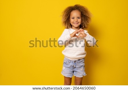 Love sign. Cute little girl makes a heart with her fingers isolated over yellow background.