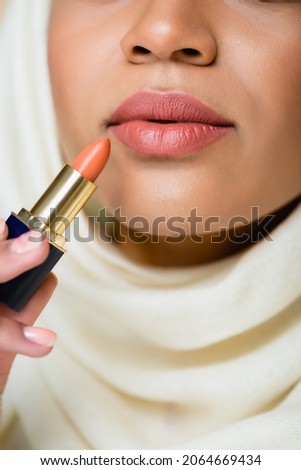 cropped view of young muslim woman in hijab applying lipstick