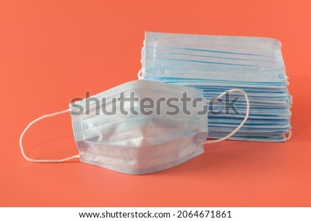 There are many new medical surgical facial three-layer masks stacked high and one mask lies next to it on a pink background