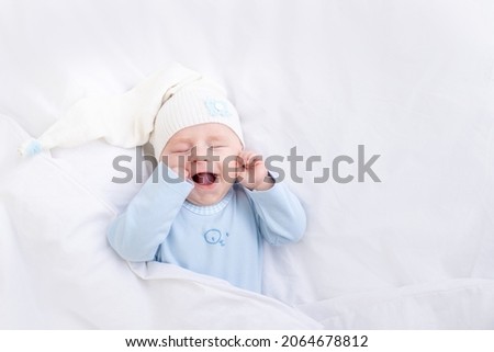 baby boy smiling in his sleep on the bed under the blanket in a cap, healthy newborn sleep Royalty-Free Stock Photo #2064678812
