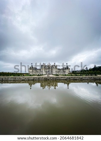 Wide angle view of Castle of Chambord in Loire valley, with its gardens, Cloudy day, water reflection, France