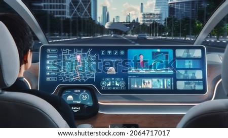 Futuristic Concept: Stylish Businessman Using Navigation App on an Augmented Reality Dashboard with Financial News Broadcast while Sitting in an Autonomous Self-Driving Zero-Emissions Electric Car. Royalty-Free Stock Photo #2064717017