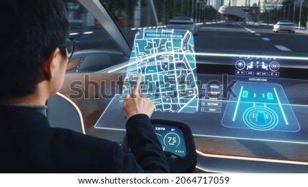Futuristic Concept: Stylish Businessman Setting Location on an Interactive Navigation App on an Augmented Reality Dashboard while Sitting in an Autonomous Self-Driving Zero-Emissions Electric Car. Royalty-Free Stock Photo #2064717059