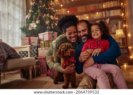 Excited girl and her family sitting on the floor near christmas tree and smiling. Mixed race family during Christmastime