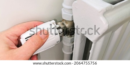 Hand regulating thermostat on district heating radiator Royalty-Free Stock Photo #2064755756