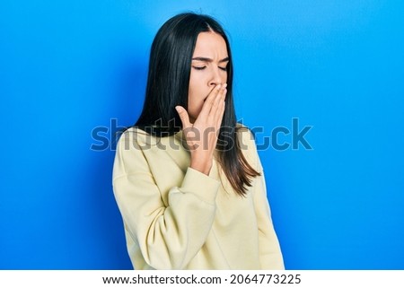 Young brunette woman wearing casual sweatshirt bored yawning tired covering mouth with hand. restless and sleepiness. 