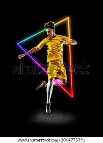 Kicking ball. Winner. Artwork of prfessional male football player in motion over neon geometric element isolated on black background. Concept of action, movement, sport, motivation. Copy space for ad