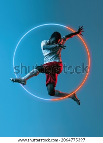 Sport competition. Artwork of prfessional male football player in motion over neon geometric element isolated on blue background. Concept of action, movement, sport, motivation. Copy space for ad