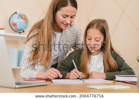 Young caucasian teacher mother tutor babysitter nanny helping her daughter schoolgirl student with homework, school project, preparing for test exam at home. Royalty-Free Stock Photo #2064776756